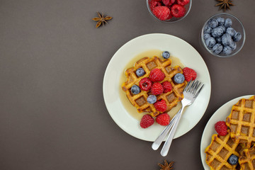 Fototapeta na wymiar Belgian, carrot waffles with maple syrup and fresh raspberries, blueberry, cinnamon and star anise . Dark background. Top view. Copy space.