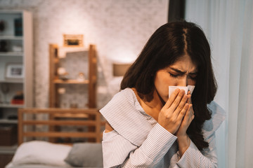 Young Asian woman suffering from cold and illness on bed with tissue at home in bedroom at night. Cold, flu, influenza illness concept