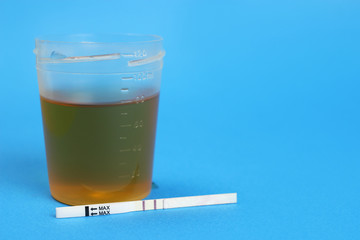 Positive ovulation test and a urine container. Copy space