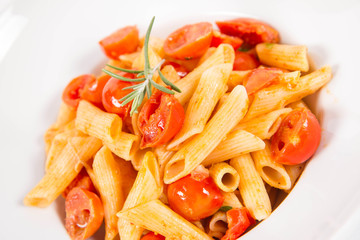 Penne with tomatoes, garlic and mozzarella decorated with rosemary twig, on a white background