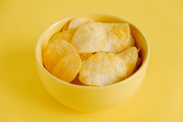 Potato chips in a yellow bowl on a yellow background. Copy, empty space for text