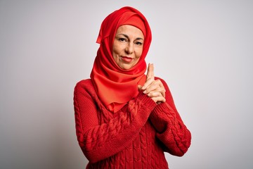 Middle age brunette woman wearing muslim traditional hijab over isolated white background Holding symbolic gun with hand gesture, playing killing shooting weapons, angry face