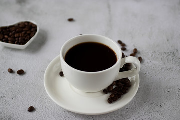 White cup with black coffee and coffee beans on a concrete. Soft focus.