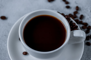 White cup with black coffee and coffee beans on a concrete. Soft focus.