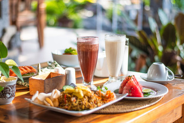 Balinese breakfast served on a table with food, fruits and colourful smoothie