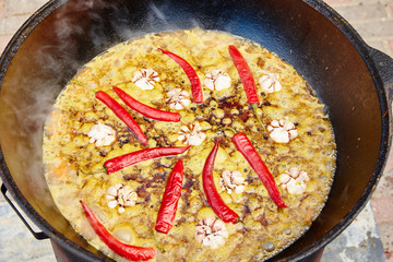 National Uzbek dish pilaf, pilaw, plov, rice with meat in big pan. Cooking process in a cauldron on fire. Preparation stage. pour out rice, Add waters, red pepper and the whole garlic
