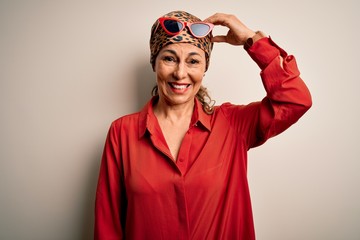 Middle age brunette woman wearing handkerchief on head and shirt over white background confuse and wonder about question. Uncertain with doubt, thinking with hand on head. Pensive concept.