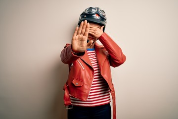 Middle age motorcyclist woman wearing motorcycle helmet and jacket over white background covering eyes with hands and doing stop gesture with sad and fear expression. Embarrassed and negative concept.