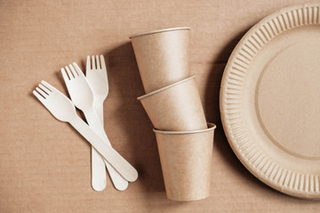 Fototapeta na wymiar Wooden forks and paper cups with plates on kraft paper background. Eco friendly disposable tableware. Also used in fast food, restaurants, takeaways, picnics. Top view. Copy, empty space for text