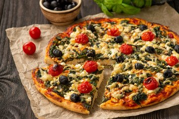 Homemade pizza with spinach, tomatoes and olives.