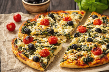 Homemade pizza with spinach, tomatoes and olives.