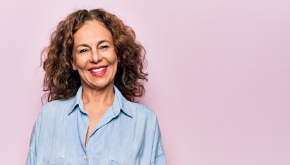 Middle age beautiful woman wearing casual denim shirt standing over pink background with a happy...