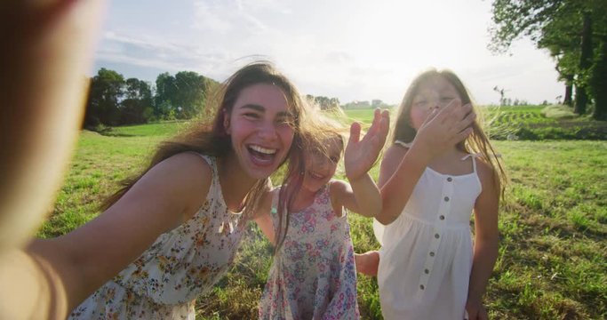 Authentic shot of happy carefree young mother and her little daughters making a selfie or video call to father or relatives on a green nature in a sunny day. Concept: technology, family, connection