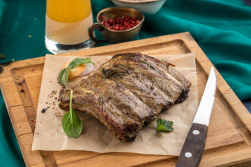 Juicy Grilled Pork Ribs Meat on Wooden Board with glass of beer on green background