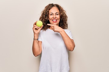 Middle age beautiful  sportswoman holding tennis ball over isolated white background smiling happy pointing with hand and finger