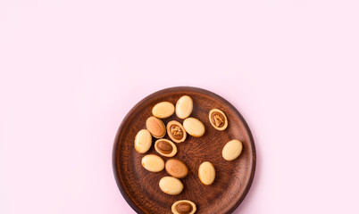 Homemade nuts with condensed milk, chocolate inside, walnuts and almonds. Dessert to tea on a plate on a light pink background.