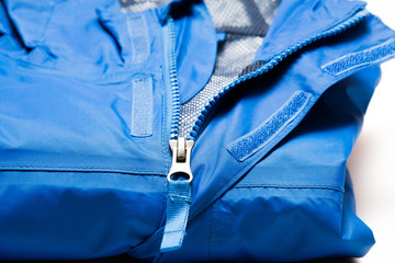 Folded blue zipper windbreaker jacket, rain proof and waterproof hiking Gore-Tex jacket hoodie. Track jacket sport nylon full zip isolated on white. Folded clothes. Outer layer garment for travel. © cattyphoto