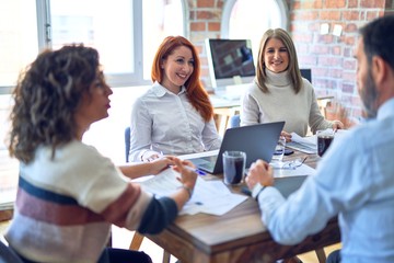 Group of business workers smiling happy working together. Sitting with smile on face using laptop reading documents at the office