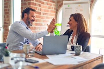 Two middle age business workers smiling happy and confident. Working together with smile on face hand giving high five at the office