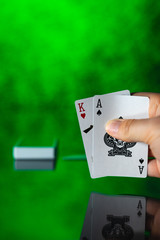 Hand showing two poker cards on the table with reflection on green background