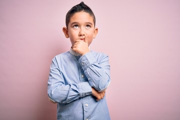 Young little boy kid wearing elegant shirt standing over pink isolated background with hand on chin thinking about question, pensive expression. Smiling with thoughtful face. Doubt concept.