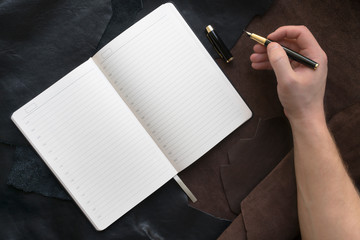 male hand holds a fountain pen, near an open notebook on a leather background. workplace concept