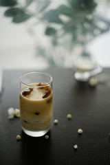 Ice coffee in glass on the dark wooden table with leafs behind