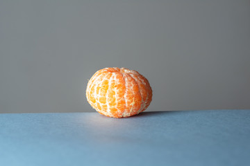 Orange tangerine without skin on a neutral blue and gray horizontal background.