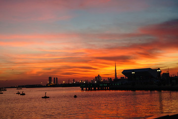 Naklejka premium Beautiful view of Dubai skyline with reflection in the golf water with amazing colors from a red warm sunset. Concept of beautiful times.