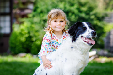 Cute little toddler girl playing with family dog in garden. Happy smiling child having fun with dog, hugging playing with ball. Happy family outdoors. Friendship between animal and kids