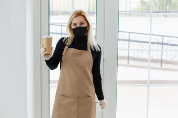 Young woman in apron with coffee on gray background. Barista concept