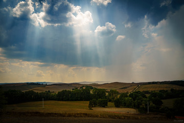 Naklejka premium Beautiful wide angle view of the Tuscany hills and fields with cumulus clouds at noon on the hot summer day