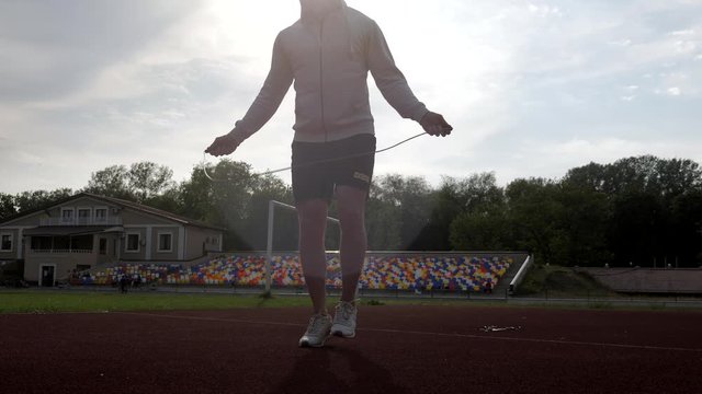 silhouette of a runner warming up jumping with a jumping rope in the park in sunset