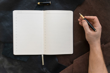 male hand holds a fountain pen, near an open notebook on a leather background. workplace concept