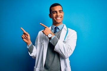 Handsome african american doctor man wearing coat and stethoscope over blue background smiling and looking at the camera pointing with two hands and fingers to the side.