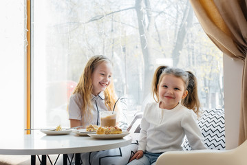 Two cute little girls are sitting in a cafe and playing on a Sunny day. Recreation and lifestyle.