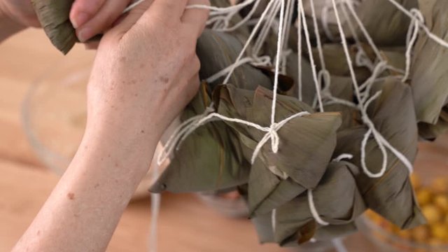 Making Zongzi - Family Preparing, Wrapping Bunch Of Chinese Rice Dumpling Zongzi Food Together On Wooden Table At Home For Dragon Boat Festival Celebration, Close Up, Lifestyle.