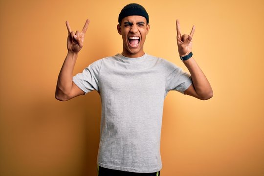 Handsome african american sportsman doing sport wearing sportswear over yellow background shouting with crazy expression doing rock symbol with hands up. Music star. Heavy music concept.