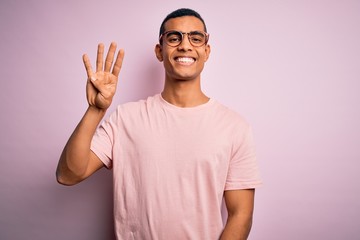 Fototapeta premium Handsome african american man wearing casual t-shirt and glasses over pink background showing and pointing up with fingers number four while smiling confident and happy.
