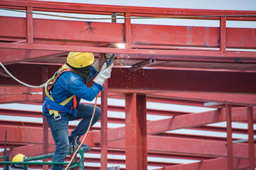 Low angle view of construction worker with hat on scaffolding is welding metal of building...