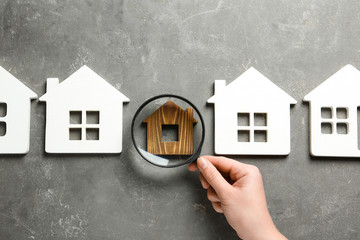 Woman with magnifying glass exploring different house models on grey stone background, top view....