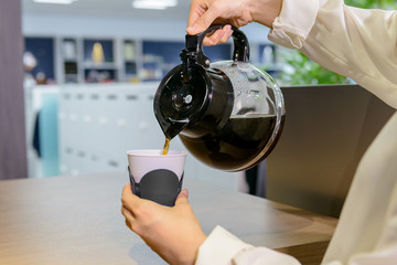 オフィスでコーヒーポットからカップにコーヒーを注ぐシーン