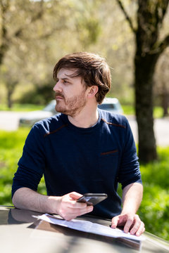 Person referencing map while holding smart phone outdoors near cars