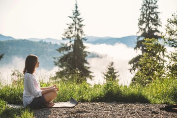 Young woman practicing yoga and sitting among grass in sunny light on background of morning mountains. Meditation. Calm tranquil moment, connection with nature.Zen. Copy space