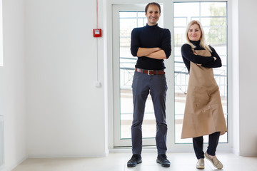 Fototapeta premium Coffee Business Concept - Barista couple in apron looking at camera ready to give Coffee Service at the modern coffee shop