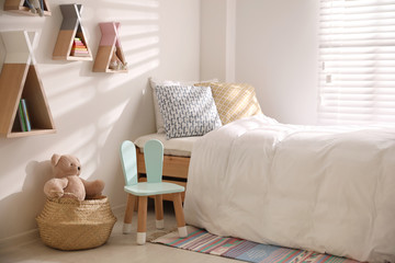 Cute little chair with bunny ears near bed indoors. Children's room interior