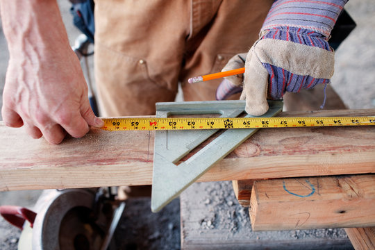 Closeup of male construction worker measuring wood for cut