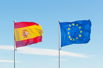 Spain and Europe EU flags on flag poles waving against sky background