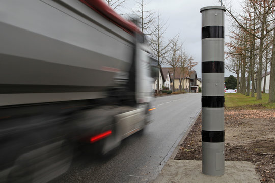 Station&auml;re Blitzers&auml;ule mit vorbeifahrendem Lkw an einem Ortseingang.