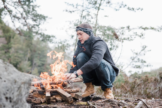 man putting sticks on a campfire outdoors in Sweden